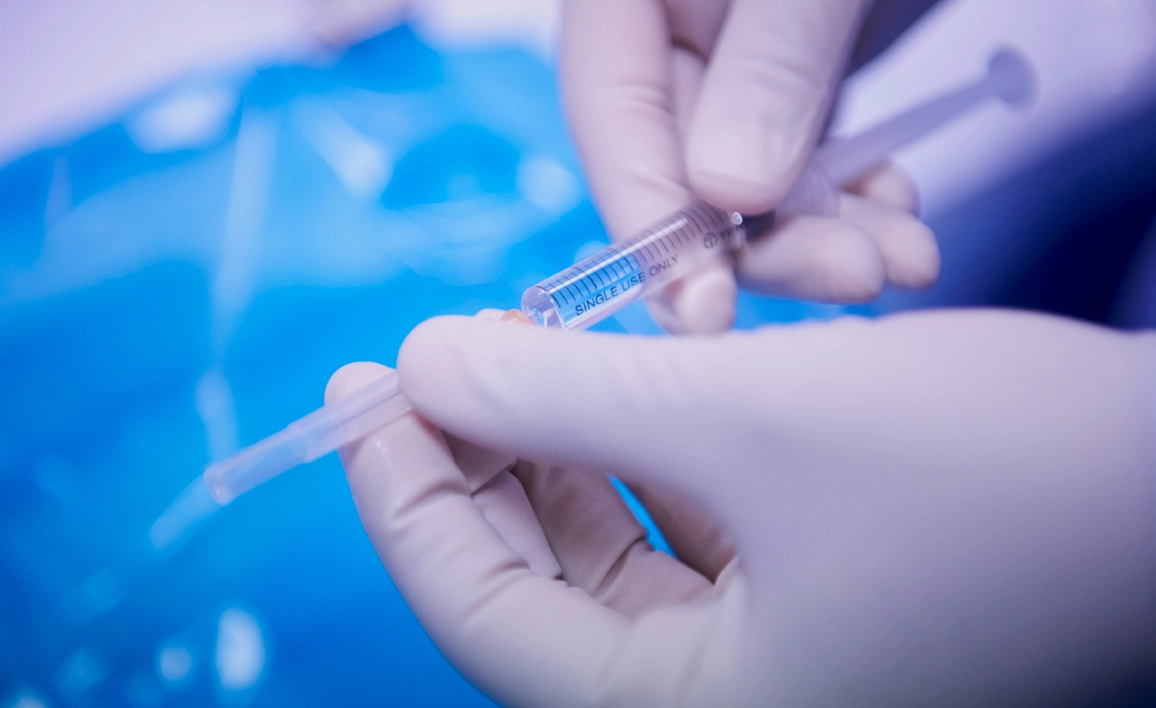 Gloved hands holding needle with liquid inside