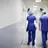 a male and female doctor in scrubs walk down a hospital corridor, away from the camera