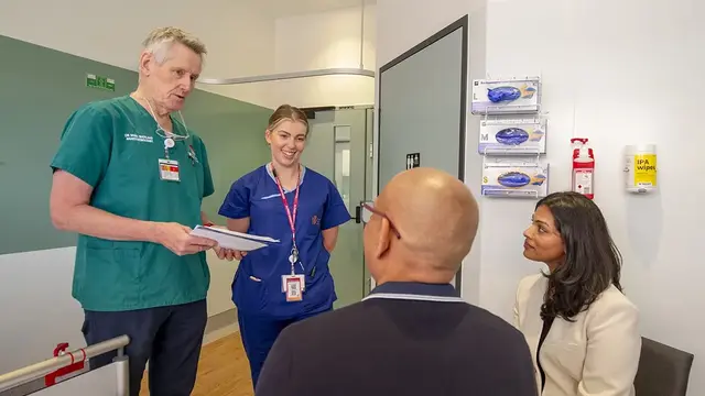 A healthcare team, including a doctor and a nurse, having a discussion with two seated individuals in a clinical setting.