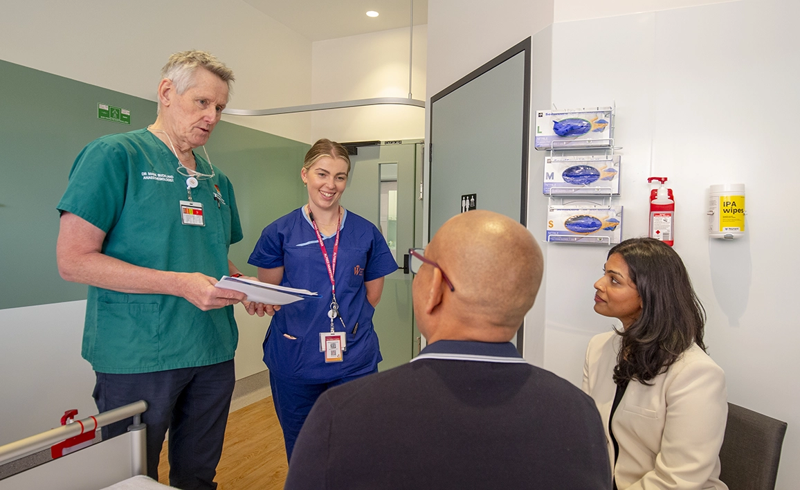 A healthcare team, including a doctor and a nurse, having a discussion with two seated individuals in a clinical setting.