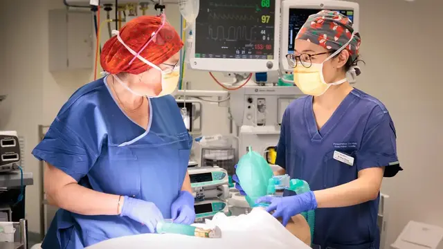 Two people in scrubs looking at each other while one uses a mask on a simulation patient