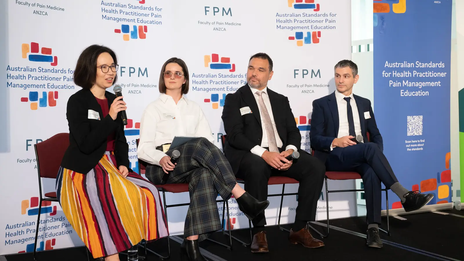 A photo of a speaking panel in front of an FPM and Education standards media wall