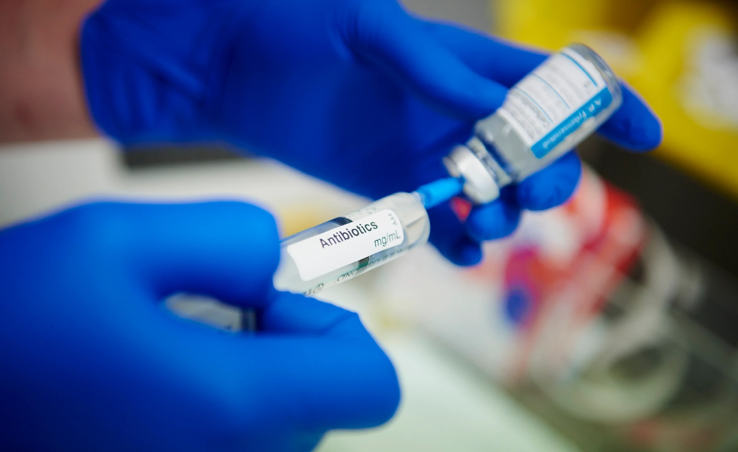 Gloved hands drawing up needle of medicine that says antibiotics