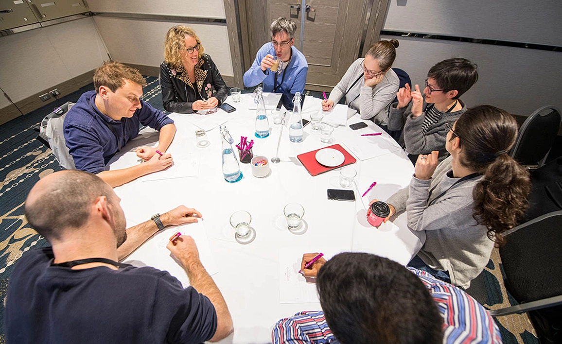 A group of professionals engaged in a discussion around a table, taking notes and collaborating in a meeting setting