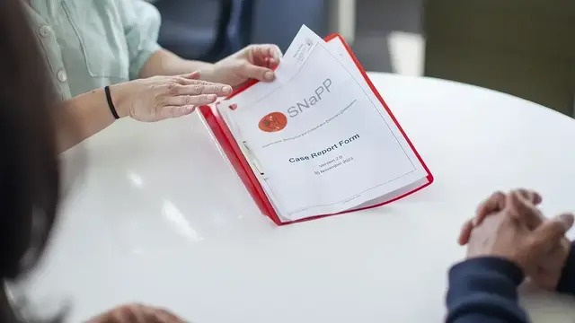 A close-up of a case report form for the SNaPP study, presented in a red folder during a discussion.