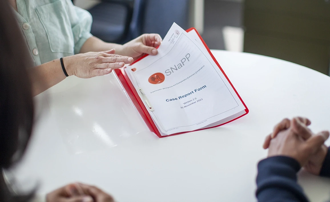 A close-up of a case report form for the SNaPP study, presented in a red folder during a discussion.