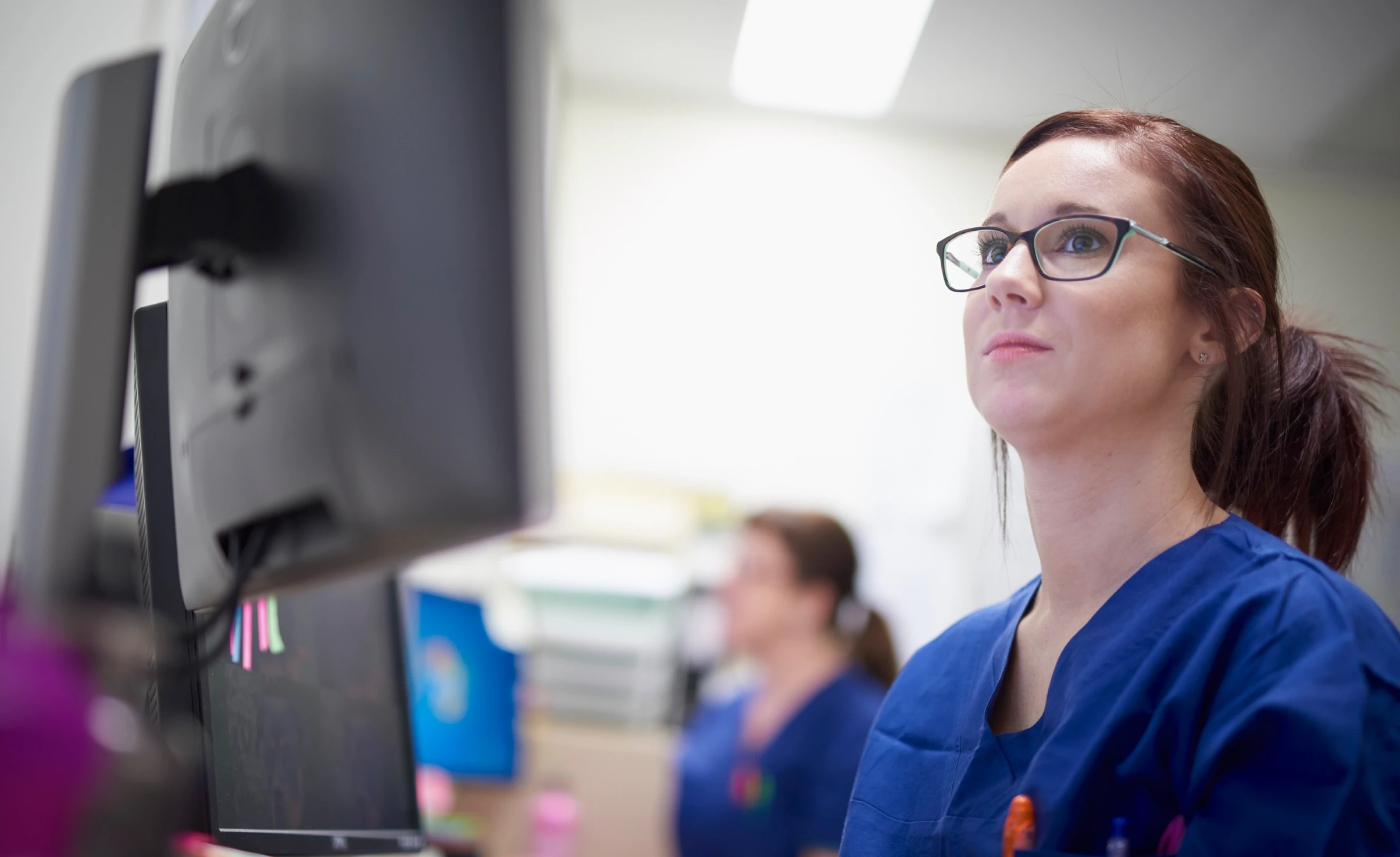 Person in scrubs and wearing glasses looking at computer screen