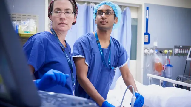 Two people in scrubs using ultrasound machine on patient and looking at monitor