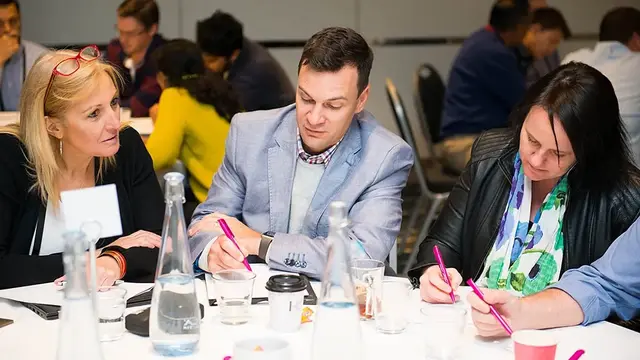 A group of professionals at a round table, engaged in discussion and note-taking at a table.