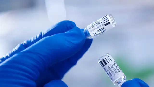 Photo of two hands holding vials of medicine