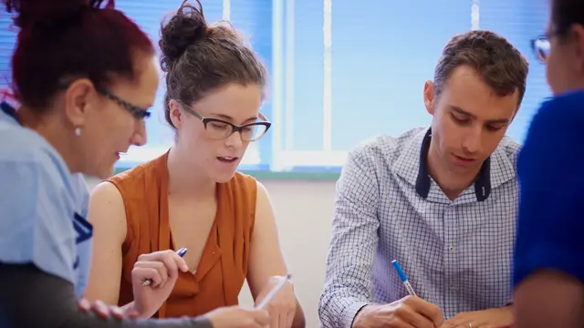 Four people looking down at some paper with pens in their hands