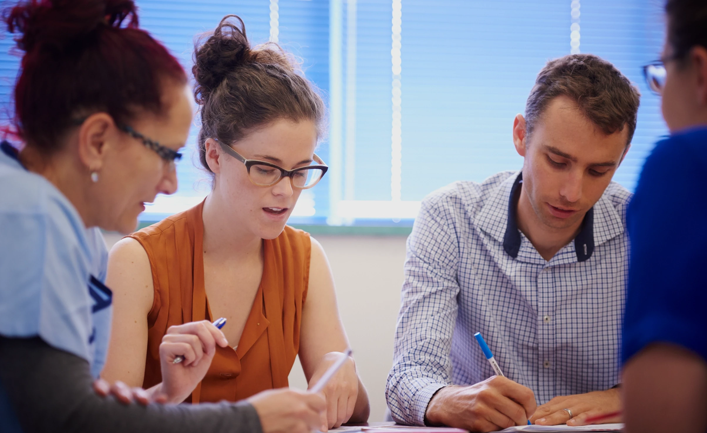 Four people looking down at some paper with pens in their hands