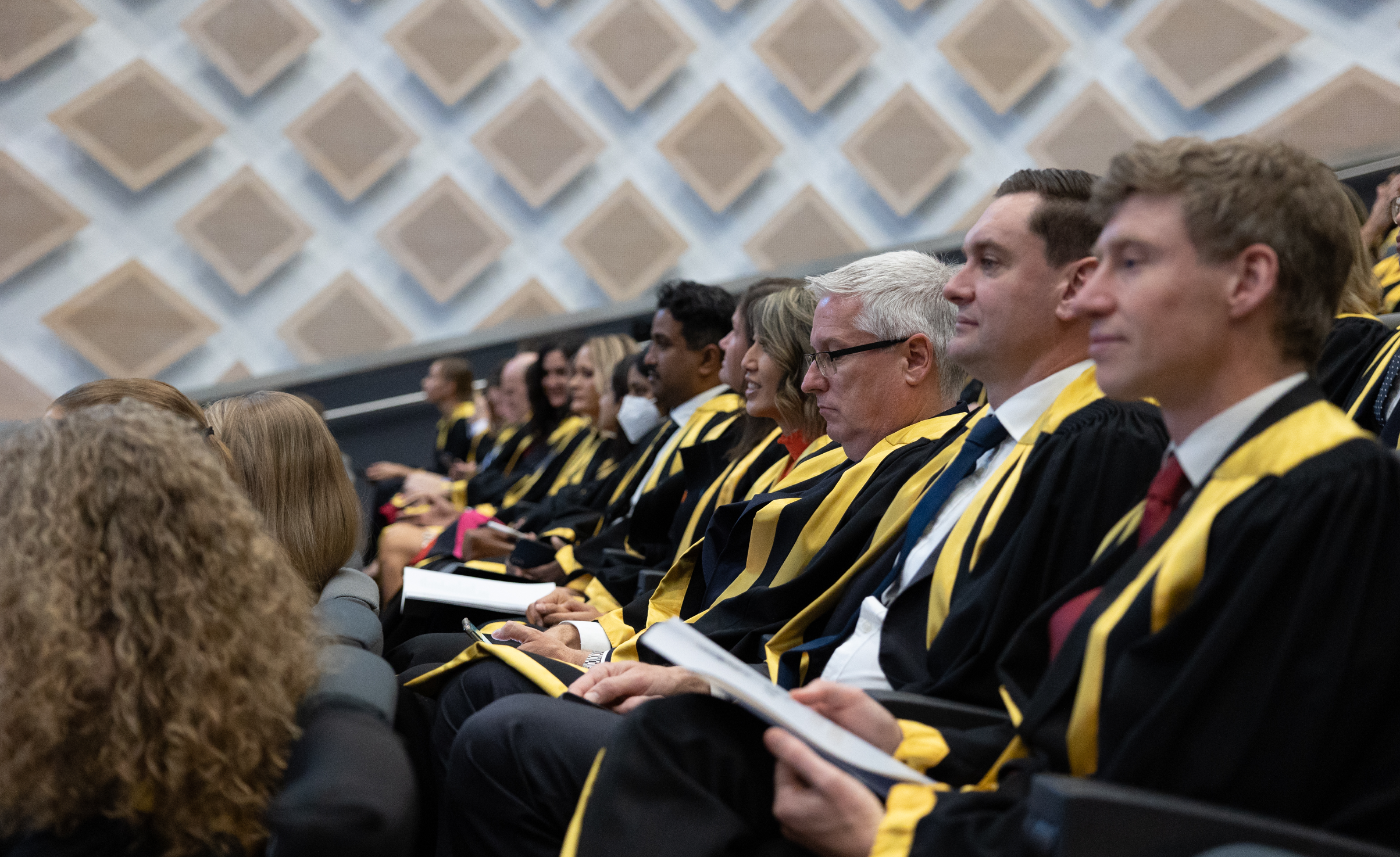 ANZCA fellows sitting in a row in their fellowship gowns with a booklet in their hands